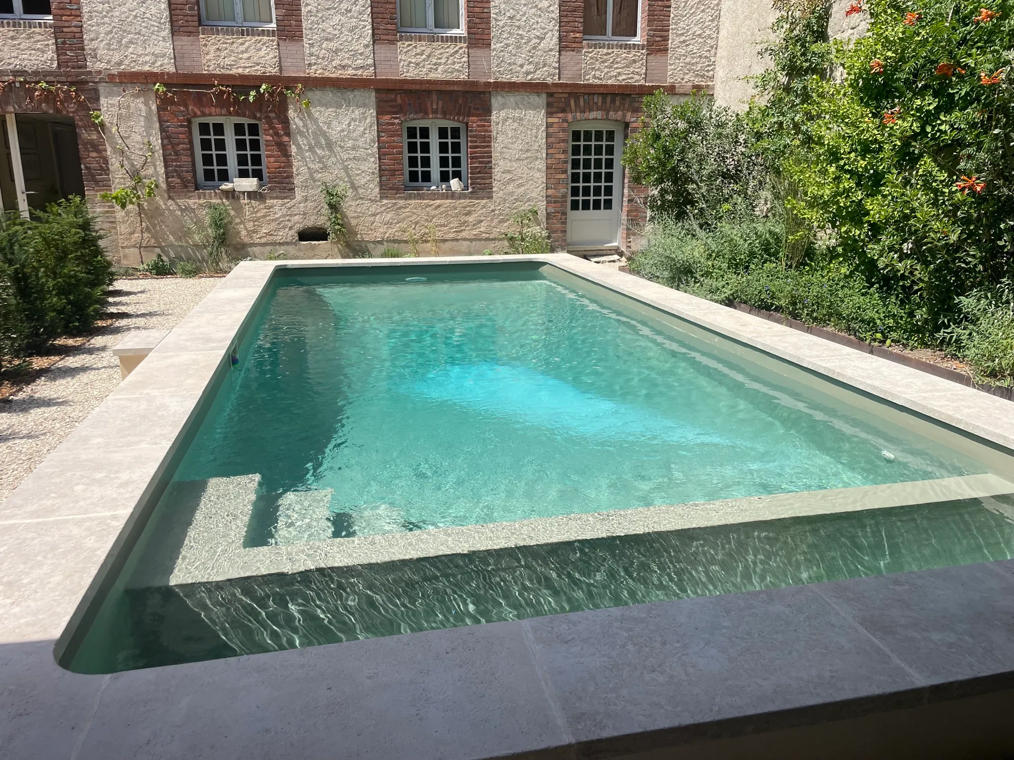 Bassin terminé en eau, margelles en pierre, jardin planté