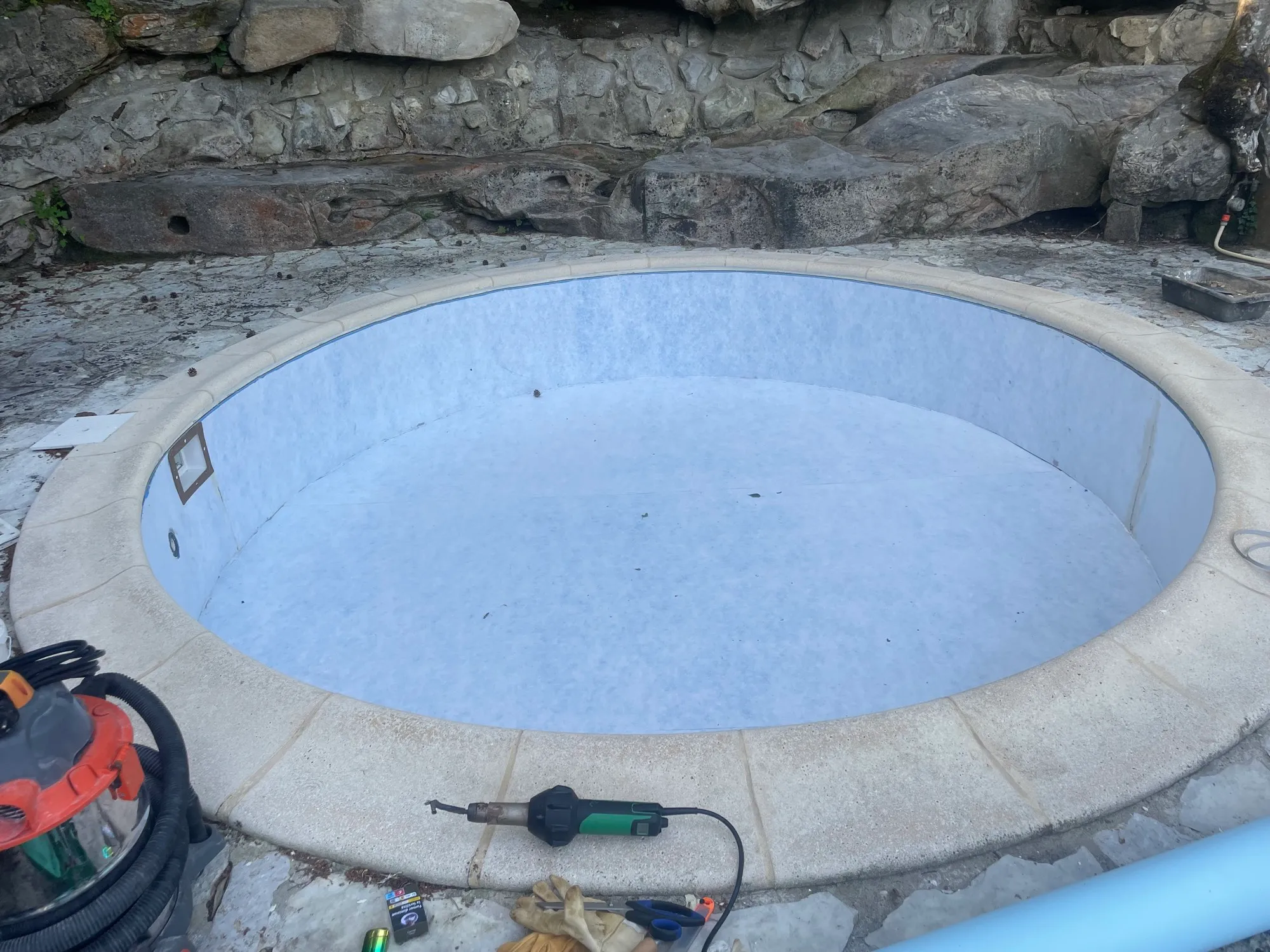 Petit bassin rond revêtu gris, margelle en pierre, mur rocheux