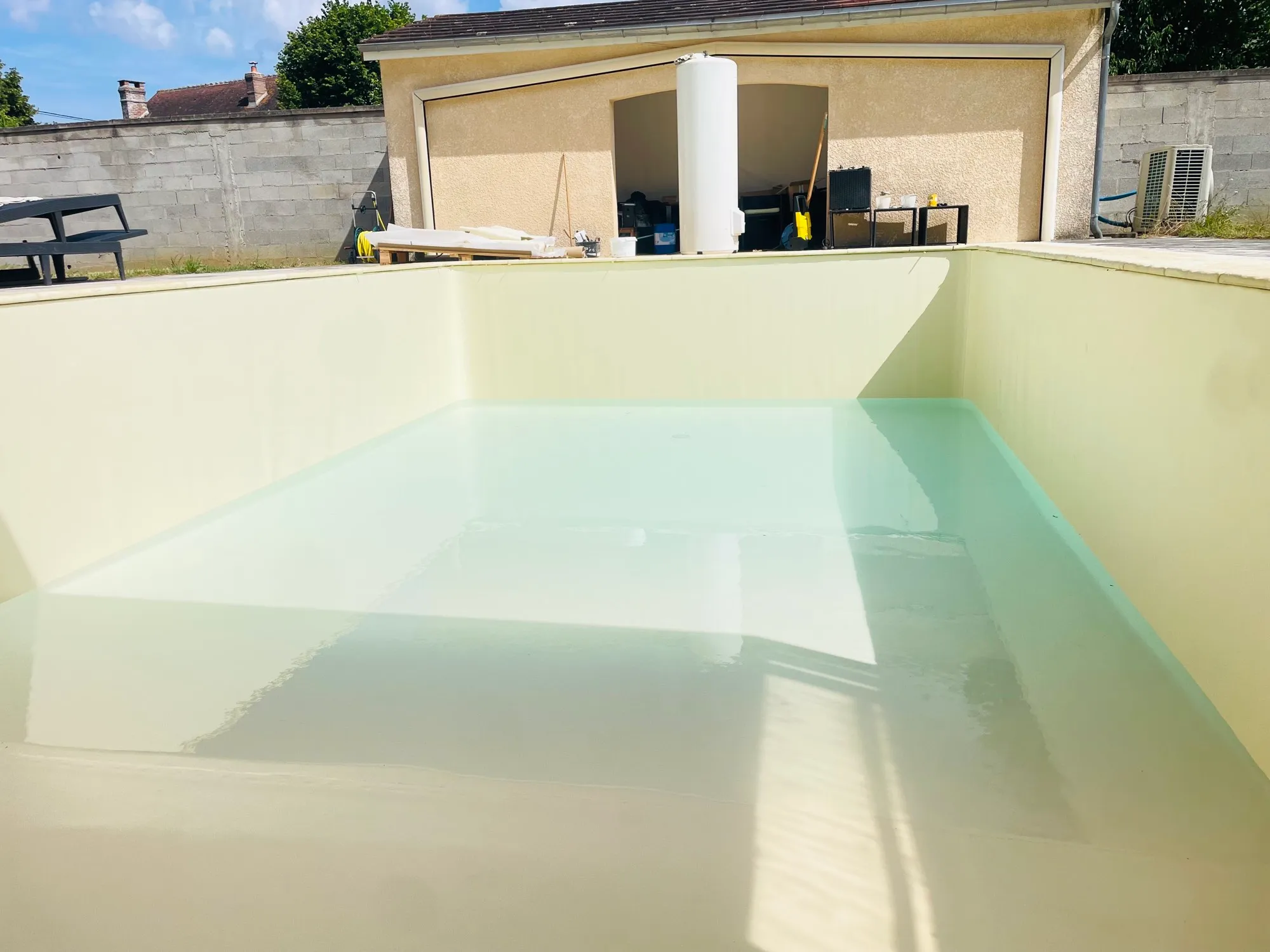 Bassin en liner crème avec fond d’eau, mur de clôture et dépendance