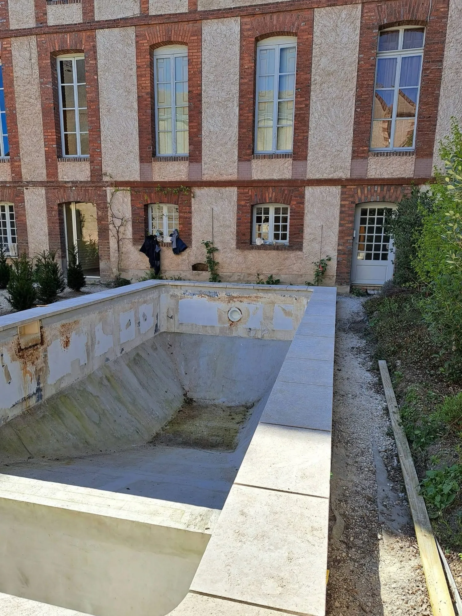 Ancien bassin béton taché, plages en pierre neuves posées